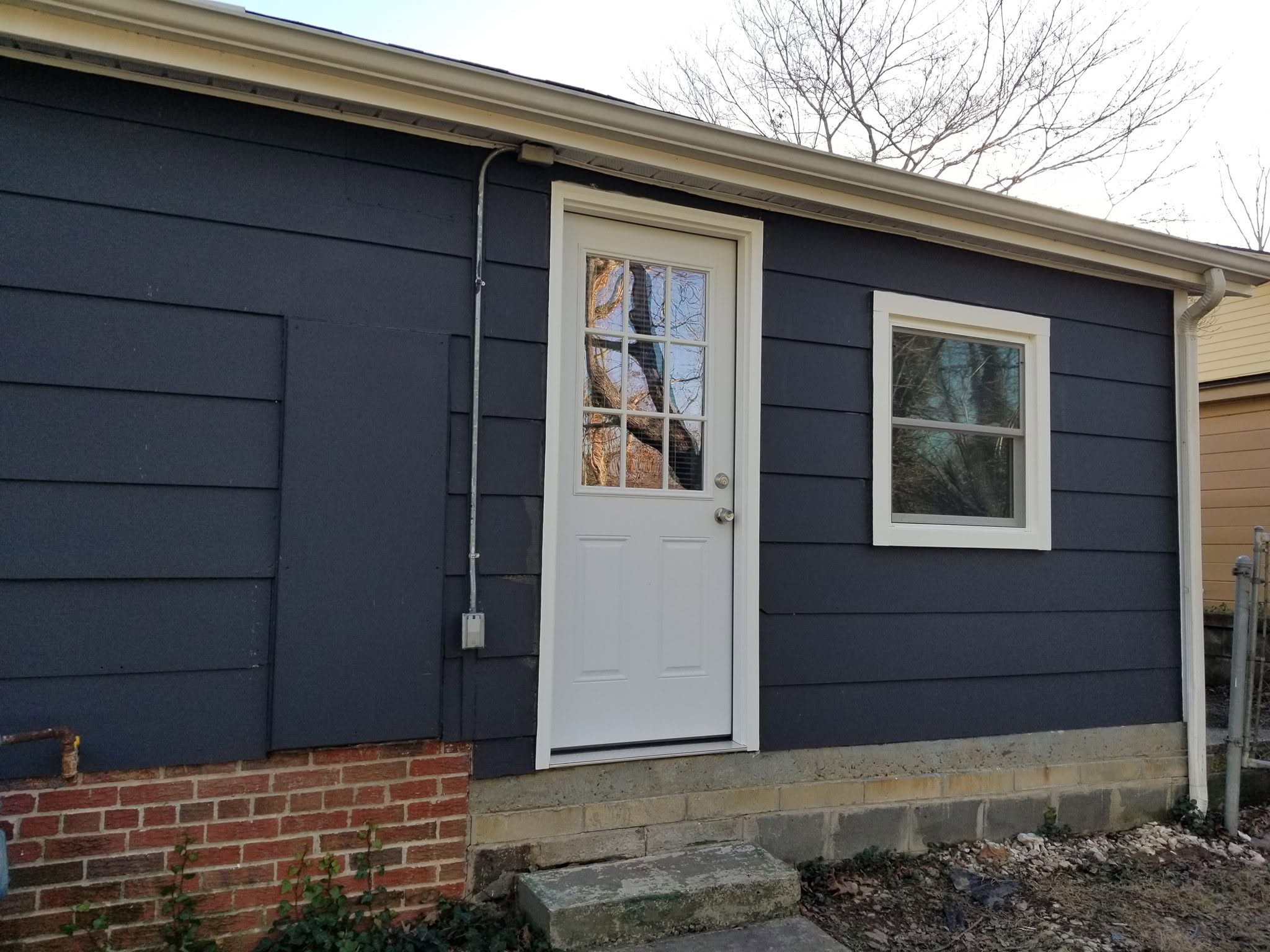 Full exterior renovation with new charcoal fiber-cement lap siding, white trim, and preserved brick base